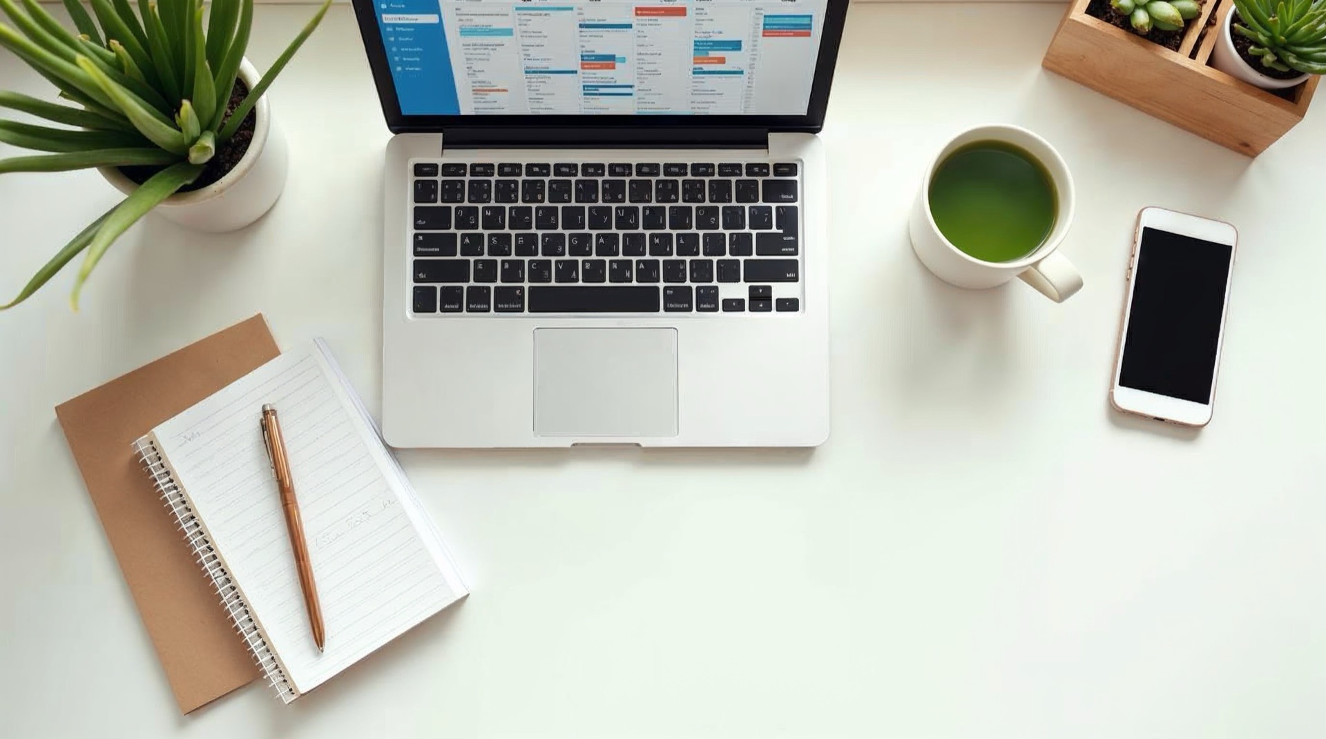 A clean, organised workspace with laptop, notepad, and green tea